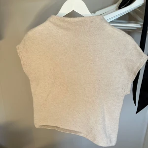 Beige stickad topp från Lindex - Säljer en stilren beige stickad topp från Lindex. Den har en enkel design med korta ärmar och en hög krage. Perfekt för lager-på-lager eller som den är. Passar till många olika stilar och tillfällen.