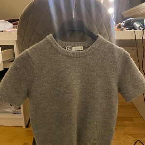 Grå stickad tröja från Zara - Säljer en stilren grå stickad tröja från Zara. Den har korta ärmar och en rund halsringning, perfekt för lager-på-lager eller som den är. Tröjan är mjuk och bekväm, idealisk för både vardag och avslappnade tillfällen.