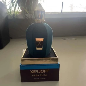 Xerjoff Erba Pura Eau de Parfum - Elegant parfymflaska från Xerjoff i en djupblå nyans med gulddetaljer. Flaskan har en lyxig design med en distinkt form och en gyllene kork. Perfekt för den som söker en exklusiv doftupplevelse. Knappt änvänd. OBS mötts bara i Nacka fraktar inte!