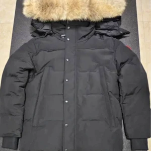 Svart dunjacka från Canada Goose - Säljer en svart dunjacka från Canada Goose med en stor pälsfodrad huva. Jackan har långa ärmar och knappar framtill. Perfekt för kalla vinterdagar.