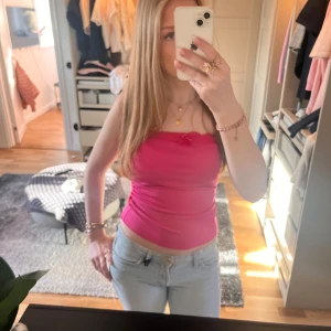 Rosa ribbad tubtopp - Säljer en snygg rosa ribbad tubtopp med spetsdetaljer och en liten rosett framtill. Perfekt för sommardagar och kan enkelt matchas med jeans eller kjol.