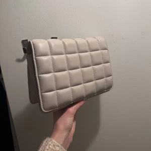 Väska från h&m - Ljusgrå/beige väska från hm! Sparsamt använd och i bra skick! Axelbandet går att ändra lite i storleken med hjälp av knäppet. Finns en ficka i väskan med dragkedja. Skick 9/10🌸