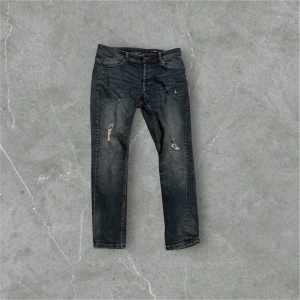 Blåa jeans från Only & Sons - Snygga grå jeans från Only & Sons med slitna detaljer och en klassisk femficksdesign. De har en normal passform och är perfekta för en avslappnad stil. Märkeslappen i brunt läder ger en extra touch.