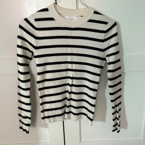 Randig ribbad tröja från Zara - Säljer en stilren ribbad tröja från Zara i svart och beige med klassiskt randigt mönster. Tröjan har långa ärmar och en rund halsringning. Perfekt för en avslappnad och trendig look. Är som en xs