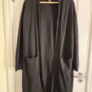 Svart cardigan jacka från Lindex - Säljer en stilren svart cardigan jacka från Lindex. Den har en öppen design med långa ärmar och praktiska fickor framtill. Perfekt för lager-på-lager under kyligare dagar.