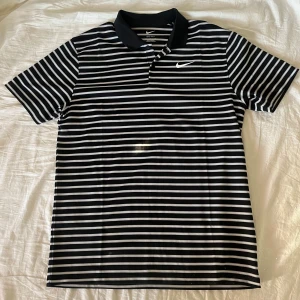 Svartvit randig golf pikétröja från Nike - Säljer en stilren svartvit randig golf piké från Nike. Helt oanvänd, fick i julklapp men passar inte mig. Den är för stor på mig, är 183 cm