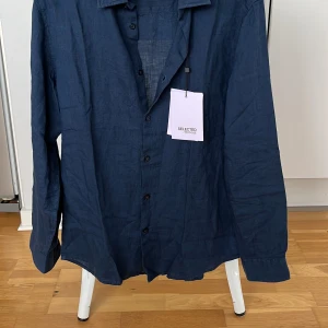 Mörkblå linneskjorta från Selected Homme - Snygg mörkblå skjorta i linne från Selected Homme. Skjortan har långa ärmar och knappar framtill. Perfekt för en stilren look. Aldrig använd med lappen kvar. Passar även M . Nypris (600)