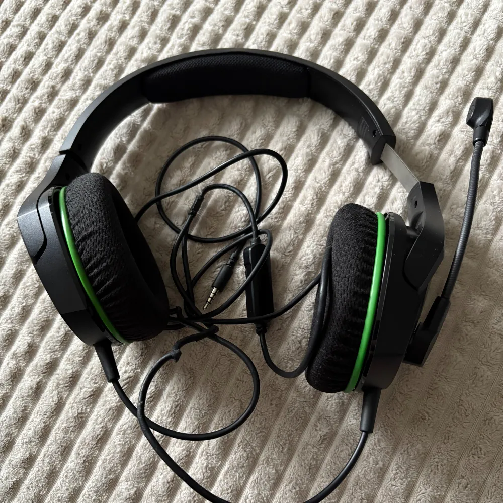 Säljer ett HyperX gamingheadset med mikrofon. Svart design med gröna detaljer och vadderade öronkuddar för komfort. Utrustad med en flexibel mikrofon och en kontroll på sladden för volymjustering. Perfekt för gaming och kommunikation.. Muu.