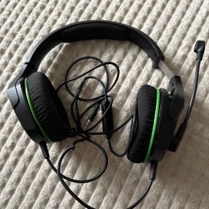 HyperX gamingheadset med mikrofon - Säljer ett HyperX gamingheadset med mikrofon. Svart design med gröna detaljer och vadderade öronkuddar för komfort. Utrustad med en flexibel mikrofon och en kontroll på sladden för volymjustering. Perfekt för gaming och kommunikation.