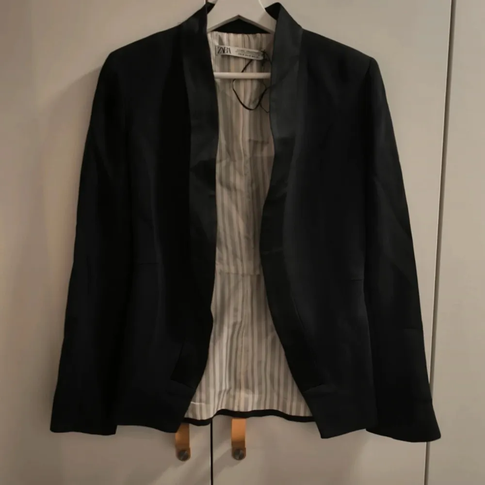 Elegant svart kavaj från Zara med pärlknappar på ärmsluten. Kavajen har en stilren design med randigt foder och är perfekt för en sofistikerad look. Från S/S 2022-kollektionen.. Puvut & Bleiserit.