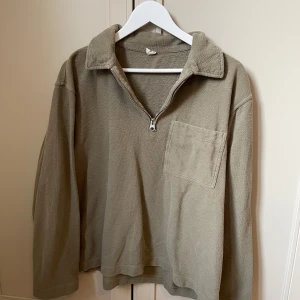 Grön tröja med dragkedja - Säljer en grön tröja med dragkedja och krage. Tröjan har en bröstficka och långa ärmar, perfekt för en avslappnad stil. Från Arket