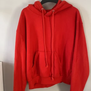 Röd hoodie från Weekday - Säljer en snygg röd hoodie från Weekday i storlek XS. Den har en stor ficka framtill och luva. Har en fläck på ryggen som knappt syns som du ser på en av bilderna. Är även lite större i storleken. Hör av dig om du vill ha fler bilder.💓