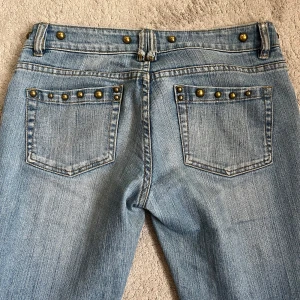 Blå jeans med nitar - Snygga blå jeans med nitar runt fickorna och midjan. De är lågmidjade och Bootcut🥰uppsprättade nedtill och en nit har lossnat men inget man tänker på💕innerbenslängden är ca 85 cm och midjemåttet är ca 38 cm❣️
