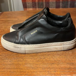 Svarta sneakers från Axel Arigato - Snygga svarta sneakers från Axel Arigato med en stilren design. Skorna har en vit sula och är tillverkade i skinn. Perfekta för en casual look.