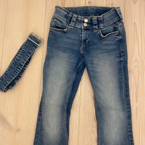 Bootcut super Low Rise jeans med + bälte - Snygga blå jeans med medföljande bälte. De har en klassisk femficksdesign och dubbla knappar i midjan. Jeansen har rivor och och det är ljusare på framsidan som gör dennnu snyggare!🥰 passar 134 - 152 men även xxs! Jag är 160 cm och dem är lite för korta för mig! Är från hm!💕💕