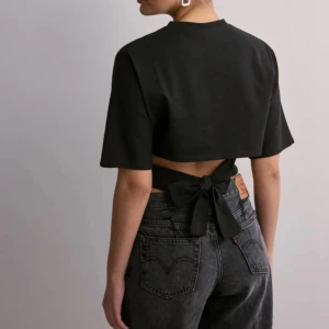 Svart open back tie tee - Snygg svart open back tie tee med korta ärmar och knytning i ryggen den passade inte mig så den är knappast använd, Den köpt från Nelly