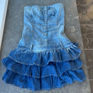 Jeansklänning med volanger - Snygg axelbandslös jeansklänning med knappar framtill och volanger. 💕det står ingen storlek men skulle uppskatta att den passar storlek S- M