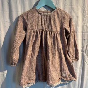 Blommig klänning från Newbie - Söt blommig klänning från Newbie i en mjuk beige ton. Klänningen har långa ärmar och fina spetsdetaljer vid halsen och fållen. Perfekt för en mysig dag med stil. 🌸