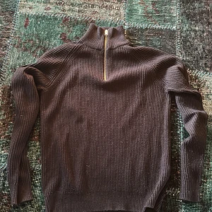 Svart ribbad tröja från Jack & Jones - Säljer en stilren svart ribbad tröja från Jack & Jones med dragkedja i halsen. Perfekt för kyligare dagar med sin långa ärmar och bekväma passform. Ett måste i garderoben för en klassisk look.