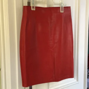 Röd skinnkjol - Snygg röd skinnkjol med dragkedja bak och en liten slits. Perfekt för att ge din outfit en edgy touch. Kjolen har en tight passform och är tillverkad i jätte mjukt äkta skinn.