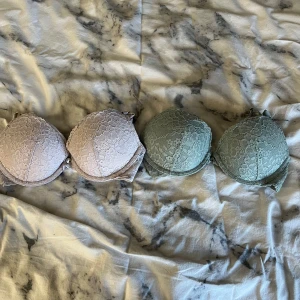 Två BH:ar i spets från H&M - Säljer två BH:ar från H&M i storlek 75A. Den ena är i en mjuk beige nyans och den andra i en dämpad grön färg. Båda har en vacker spetsdesign och justerbara axelband för bästa passform. Perfekta för att ge en romantisk touch till din garderob.