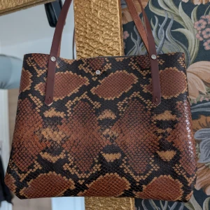Brun mönstrad axelväska - Snygg brun axelväska med ormmönster och bruna handtag. Väskan har en unik design med en kombination av olika mönster på fram- och baksidan. Perfekt för att ge en stilfull touch till din outfit. Handsydd i läderimitation.