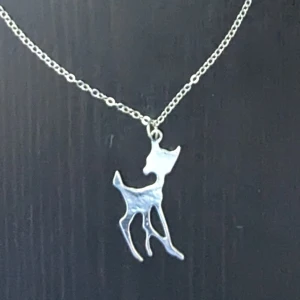 Silverhalsband med hjortberlock - Elegant silverhalsband med en stiliserad hjortberlock. Kedjan är tunn och smidig, vilket ger ett subtilt och sofistikerat intryck. Perfekt för djurälskare eller som en unik accessoar till din outfit. Passar perfekt för barn och ungdomar. Passar även vuxna, för vuxna blir det ett kort halsband.