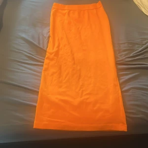 Orange långkjol - Snygg och stilren orange långkjol perfekt för sommardagar. Kjolen har en enkel design utan mönster eller detaljer, vilket gör den lätt att matcha med olika toppar. Ett måste i garderoben för en färgglad look!
