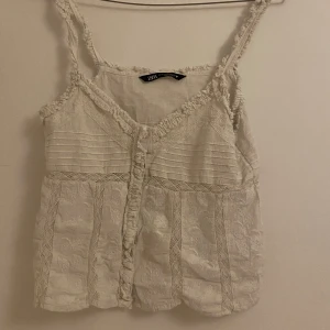 Vit spetsprydd linnetopp från Zara - Säljer en söt vit linnetopp från Zara med spetsdetaljer och broderade mönster. Perfekt för varma sommardagar! Inte använt mycket men köpt från vinted 💗