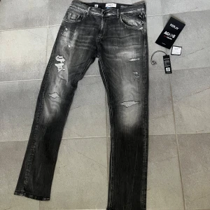 Grå jeans från Replay - Snygga grå jeans från Replay med slitna detaljer och en cool tvättad look. De har en klassisk femficksdesign och en knappgylf. Perfekta för en avslappnad stil med en touch av edge. Helt nya och oanvända, endast testade, storlek W34 L34 nypris 2500