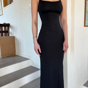 Svart långklänning från Bershka - Säljer en elegant svart långklänning från Bershka. Klänningen är ärmlös med en tight passform och har en stilren öppen rygg. Perfekt för en kväll ute eller en speciell tillställning.