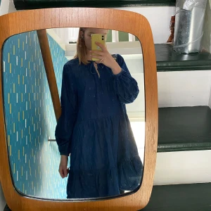 Mörkblå klänning med knytband - Säljer en mörkblå klänning med lång ärm och knytband vid halsen. Klänningen har en lös passform och volangdetaljer. Passar många olika storlekar vid frågor hör gärna av er. 