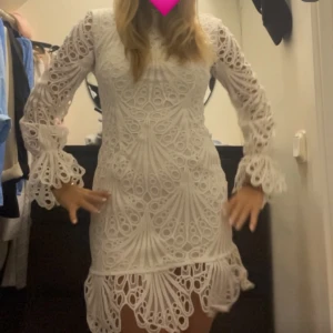 Vit spetsklänning med volangdetaljer - Säljer en elegant vit spetsklänning med långa ärmar och vackra volangdetaljer vid ärmslut och nederkant. Perfekt för speciella tillfällen så som student och midsommarfirande. Klänningen har en figurnära passform och ett intrikat mönster som ger en lyxig känsla.