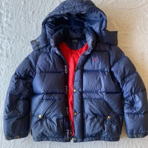 Blå dunjacka från Polo Ralph Lauren - Snygg blå dunjacka från Polo Ralph Lauren med röd insida. Passar ca 150-160 cm