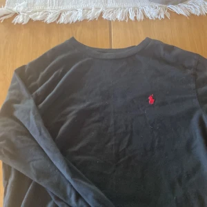 Svart långärmad tröja från Polo Ralph Lauren - Säljer en stilren svart långärmad tröja från Polo Ralph Lauren med det klassiska röda logotypbroderiet på bröstet. Perfekt för en avslappnad och snygg look.