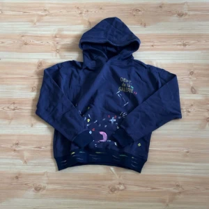  Gallery Dept. - Säljer en stilren mörkblå hoodie från Gallery Dept. med färgglada detaljer och text på framsidan. Perfekt för en avslappnad stil. Den har en klassisk huva och långa ärmar.