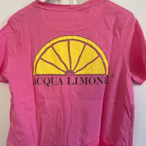 Rosa t-shirt från Acqua Limone - Säljer en snygg rosa t-shirt från Acqua Limone med deras klassiska logga på framsidan och en stor citronhalva på baksidan. Perfekt för en färgglad och avslappnad stil. 💖
