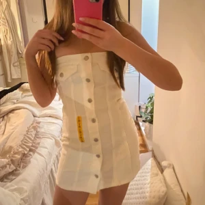 Vit axelbandslös klänning från Pull&Bear - Säljer en stilren vit axelbandslös klänning från Pull&Bear. Klänningen har knappar framtill och en figurnära passform. Perfekt för sommarens varma dagar. 🌞