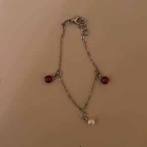 Silverfärgat armband med pärlor - Elegant silverfärgat armband med tre pärlor, två i röd nyans och en i vit. Ej nickelfritt! 