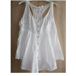 Vit ärmlös blus - Säljer en supergullig, luftig, vit ärmlös blus med knappar framtill och dekorativa spetsdetaljer. Tyvärr för tight över min byst. Storlek 38 (sitter som 36).  Sitter smickrande och tight mot kroppen samt är snyggt utgående längst ner.