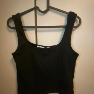 Svart ribbad linnetopp från 157 - Säljer en stilren svart ribbad linnetopp från 157. Perfekt för en enkel och snygg look. Toppen har en klassisk design med breda axelband.