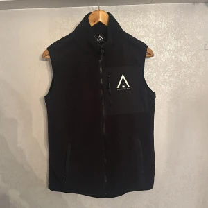 Svart Herr fleeceväst från Wearcolour - Säljer en snygg svart Herr fleeceväst från Wearcolour med dragkedja och en praktisk bröstficka. Perfekt för lager-på-lager under kyliga dagar. Västen har en stilren design med logotyp på bröstet. Den är använd ett fåtal gånger och nypris är 500kr. 