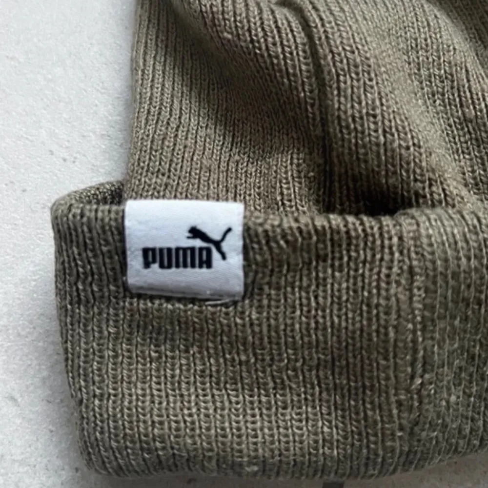 Snygg olivgrön mössa från Puma med broderad logga framtill. Tillverkad i mjukt och bekvämt material som håller dig varm under kyliga dagar. Perfekt accessoar för en sportig look. MVH EliteVolt. Asusteet.