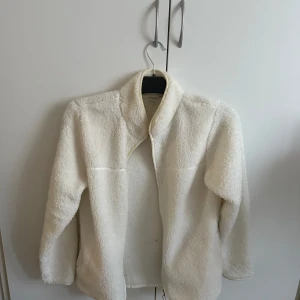 Vit teddyjacka - Mysig vit teddyjacka med dragkedja framtill. Perfekt för vårens dagar med sin mjuka och fluffiga textur. Jackan har en hög krage och långa ärmar. 
