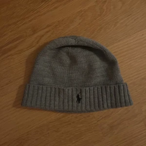 Grå stickad mössa från Ralph Lauren - Snygg grå stickad mössa från Ralph Lauren med broderad logga framtill.