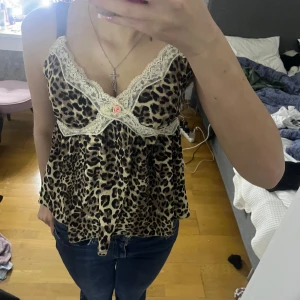 Leopardmönstrad linne med spetsdetaljer - Säljer en leopardmönstrad linne med vackra spetsdetaljer och en liten ros framtill. Toppen har smala axelband och en lös passform.