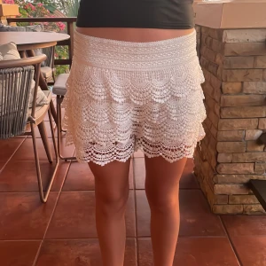 Vit spetskjol med volanger - Charmig vit kortkjol i spets med flera lager av volanger. Perfekt för en somrig look. Elastisk midja för bekväm passform.