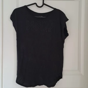 Svart t-shirt från Warp - Säljer en svart t-shirt från Warp med ett diskret tryck på framsidan. T-shirten har korta ärmar och en rund halsringning. Perfekt för en avslappnad stil.