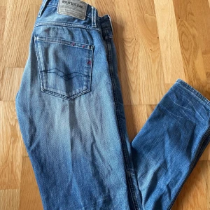 Blå jeans från Replay - Säljer ett par snygga blå jeans från Replay, modell Anbass. De har en klassisk femficksdesign med en diskret broderad detalj på bakfickan. Jeansen har en knappgylf och är i en stilren blå tvätt.