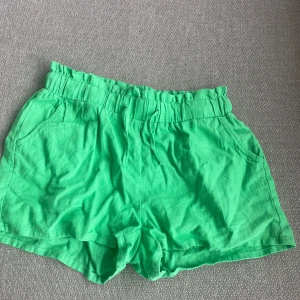 Gröna linneshorts från Lindex - Snygga gröna linneshorts från Lindex i en skön och luftig design. Använda 1 gång. Perfekta för varma sommardagar med elastisk midja för extra komfort. De har en enkel och stilren look som passar till många tillfällen. Man kan ha den både mellan midja och hög midja. Storlek 164